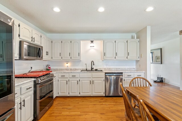 kitchen with white cabinets, light wood-type flooring, sink, and appliances with stainless steel finishes