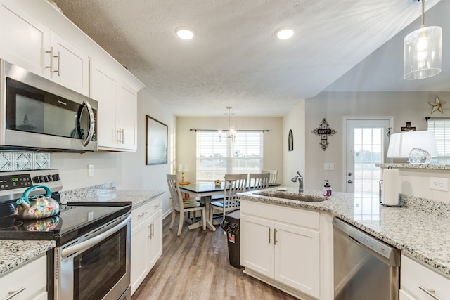 kitchen with sink, appliances with stainless steel finishes, hanging light fixtures, and white cabinets