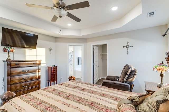 bedroom featuring a walk in closet, ensuite bath, a raised ceiling, a closet, and ceiling fan