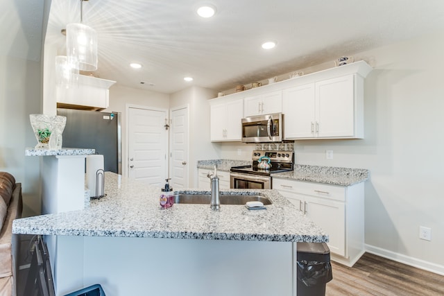 kitchen with appliances with stainless steel finishes, hanging light fixtures, white cabinets, light stone counters, and light hardwood / wood-style flooring