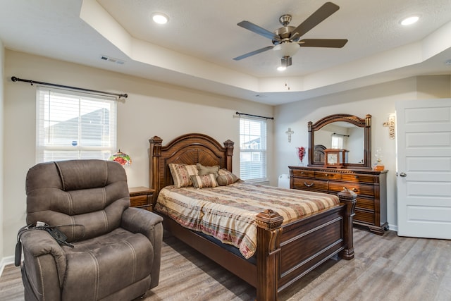 bedroom featuring light hardwood / wood-style flooring, a raised ceiling, and ceiling fan