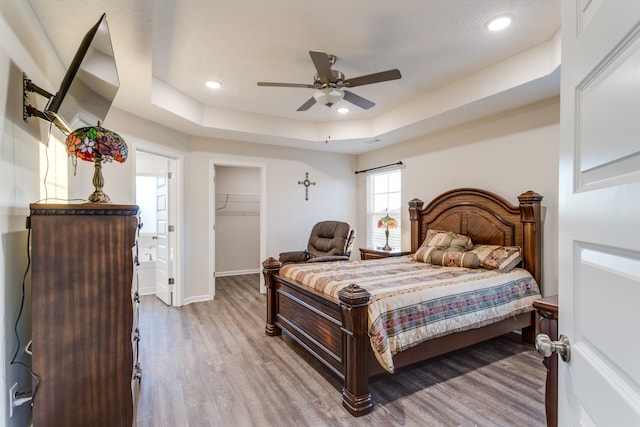 bedroom with a closet, a spacious closet, a raised ceiling, light hardwood / wood-style floors, and ceiling fan