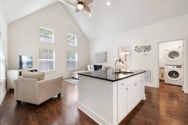 kitchen with sink, a center island with sink, high vaulted ceiling, stacked washer and clothes dryer, and white cabinets