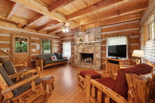 living room featuring ceiling fan, light hardwood / wood-style flooring, wooden ceiling, beamed ceiling, and a stone fireplace