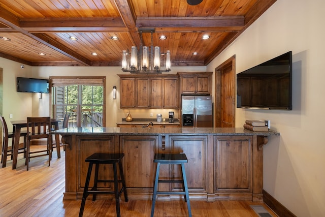 kitchen with kitchen peninsula, stainless steel refrigerator with ice dispenser, wooden ceiling, and dark stone countertops