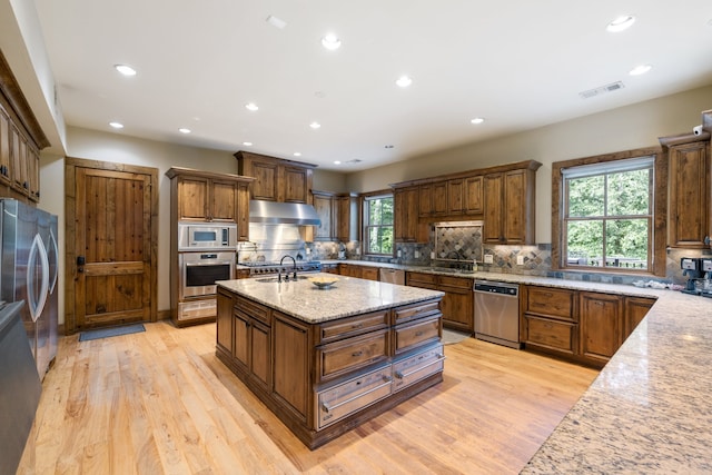 kitchen with plenty of natural light, light stone counters, an island with sink, and appliances with stainless steel finishes