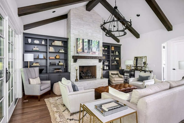 living room featuring beamed ceiling, hardwood / wood-style floors, a fireplace, and an inviting chandelier