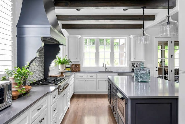 kitchen featuring sink, hardwood / wood-style floors, white cabinetry, decorative light fixtures, and beam ceiling