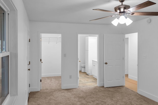 unfurnished bedroom featuring ceiling fan, a spacious closet, ensuite bathroom, light colored carpet, and a closet