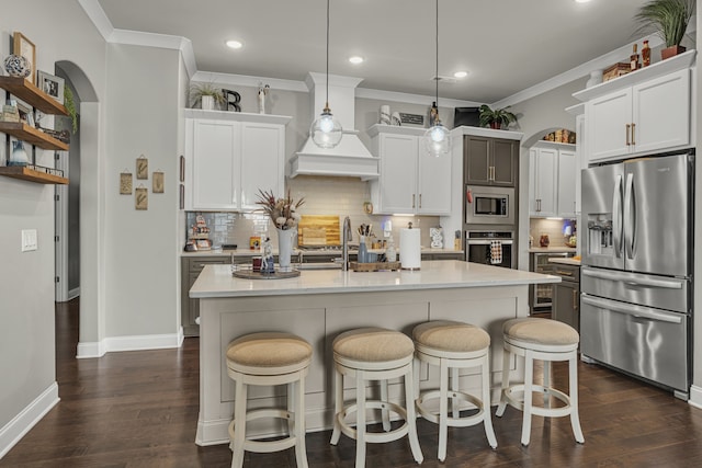 kitchen featuring appliances with stainless steel finishes, decorative light fixtures, tasteful backsplash, an island with sink, and white cabinetry