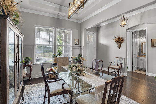 dining space with ornamental molding, dark wood-type flooring, a notable chandelier, and a tray ceiling