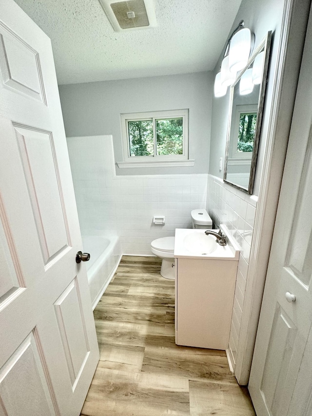 bathroom featuring tile walls, vanity, a textured ceiling, hardwood / wood-style flooring, and toilet