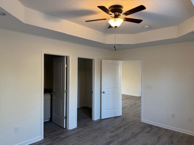 unfurnished bedroom featuring a raised ceiling, a textured ceiling, dark hardwood / wood-style flooring, a walk in closet, and a closet