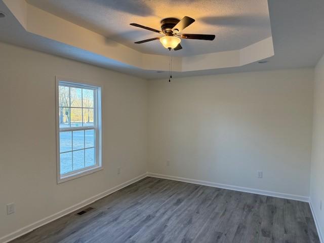 unfurnished room with dark hardwood / wood-style floors, ceiling fan, and a tray ceiling