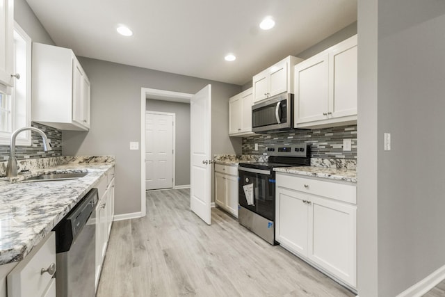 kitchen featuring light stone countertops, stainless steel appliances, backsplash, white cabinetry, and sink