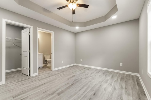 unfurnished bedroom featuring a raised ceiling, a closet, light wood-type flooring, a walk in closet, and ceiling fan