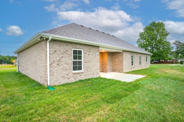 rear view of property featuring a patio area, a shingled roof, brick siding, and a yard