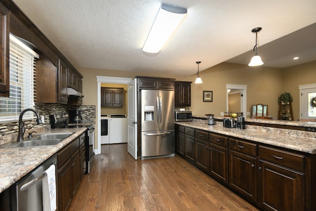 kitchen with appliances with stainless steel finishes, sink, dark wood-type flooring, decorative light fixtures, and washer and clothes dryer