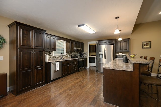 kitchen featuring a kitchen breakfast bar, kitchen peninsula, stainless steel appliances, pendant lighting, and dark hardwood / wood-style flooring