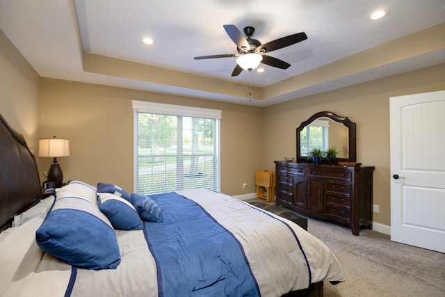 bedroom featuring ceiling fan, a tray ceiling, and light colored carpet