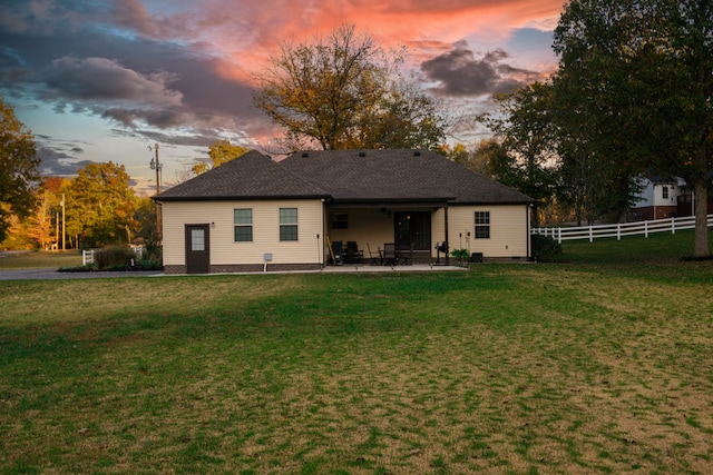 back house at dusk featuring a yard and a patio area