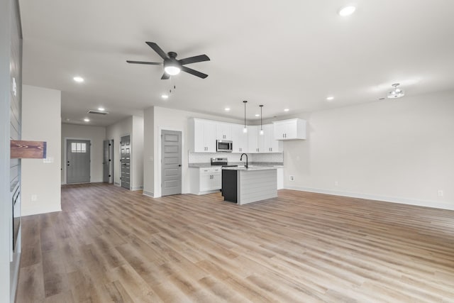 kitchen with hanging light fixtures, light hardwood / wood-style floors, a kitchen island with sink, white cabinets, and appliances with stainless steel finishes