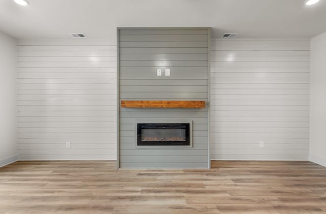 unfurnished living room with a large fireplace, light wood-type flooring, and wooden walls