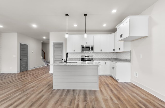 kitchen featuring a kitchen island with sink, white cabinets, sink, light wood-type flooring, and appliances with stainless steel finishes