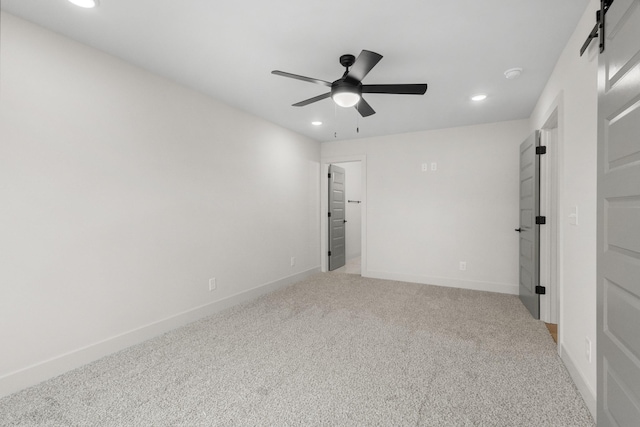 carpeted empty room featuring a barn door and ceiling fan