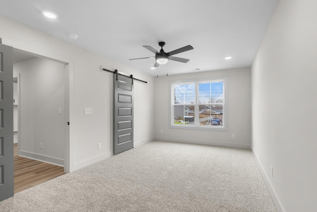 unfurnished bedroom with a barn door, light colored carpet, and ceiling fan