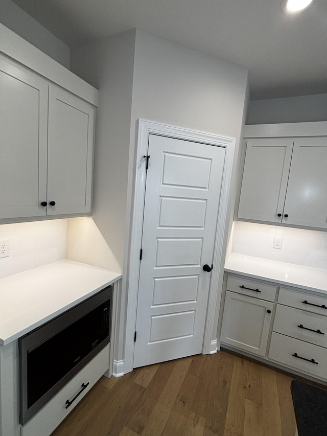 kitchen with white cabinetry, dark hardwood / wood-style flooring, decorative backsplash, and built in microwave