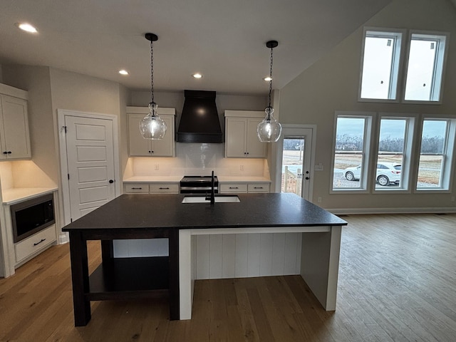 kitchen featuring premium range hood, white cabinetry, sink, and an island with sink