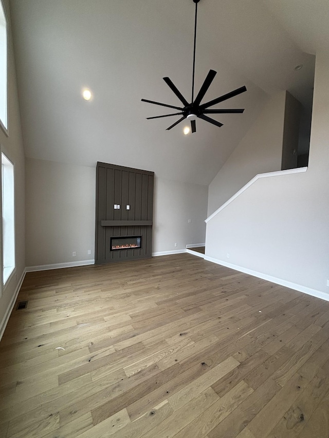 unfurnished living room featuring ceiling fan, high vaulted ceiling, a fireplace, and light hardwood / wood-style floors