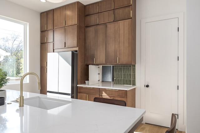 kitchen with tasteful backsplash, sink, refrigerator, and light wood-type flooring