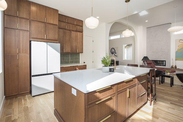 kitchen with a fireplace, a center island with sink, white fridge, and pendant lighting