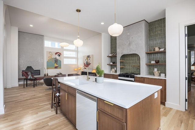 kitchen with light wood-type flooring, dishwashing machine, a kitchen island with sink, sink, and decorative light fixtures