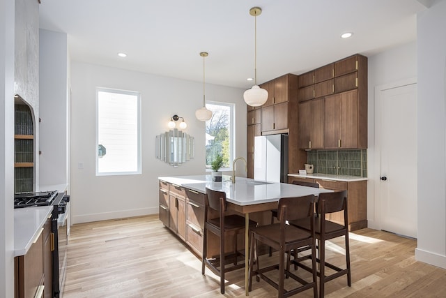 kitchen featuring stainless steel range, a kitchen breakfast bar, refrigerator, light hardwood / wood-style floors, and a center island with sink