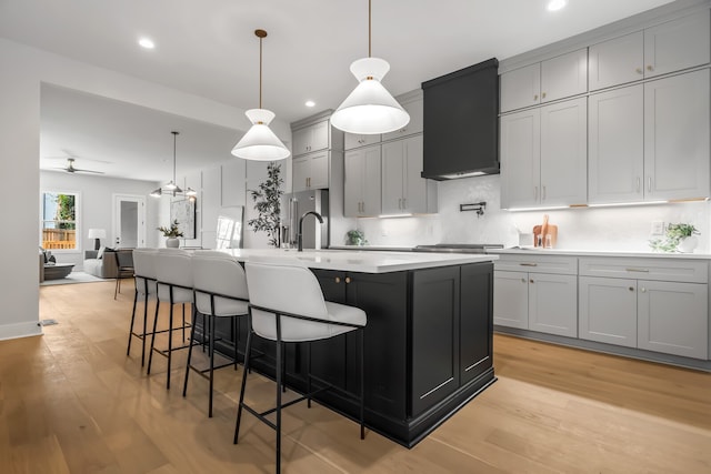 kitchen featuring gray cabinetry, light wood-type flooring, premium range hood, and hanging light fixtures