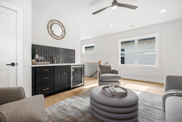 living room with light hardwood / wood-style floors, sink, beverage cooler, and ceiling fan