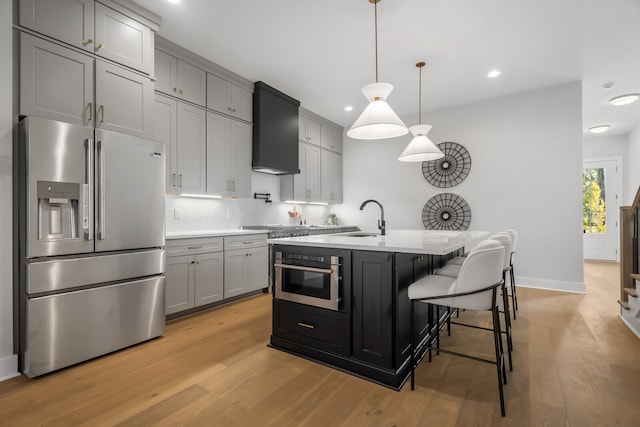 kitchen with custom range hood, gray cabinetry, stainless steel appliances, pendant lighting, and light wood-type flooring