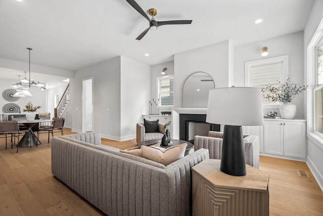 living room with light hardwood / wood-style flooring, ceiling fan with notable chandelier, and plenty of natural light