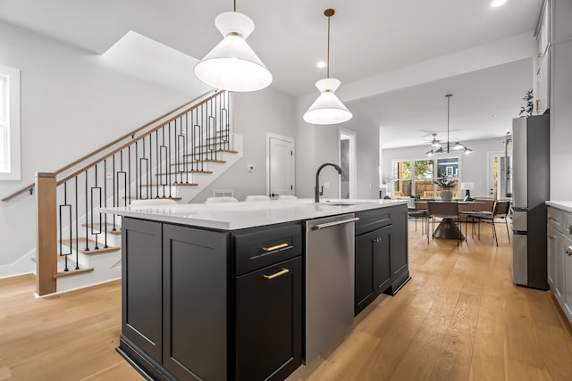 kitchen with sink, light wood-type flooring, stainless steel appliances, pendant lighting, and a center island with sink