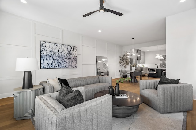 living room with sink, ceiling fan with notable chandelier, and light hardwood / wood-style floors