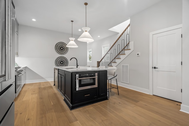 kitchen with pendant lighting, light wood-type flooring, stainless steel appliances, and an island with sink