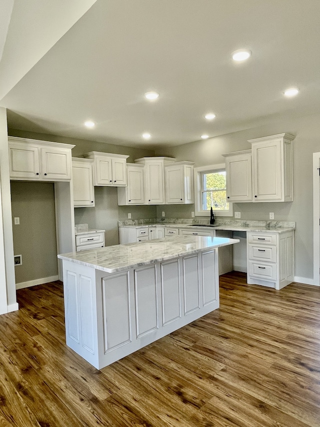 kitchen with sink, dark hardwood / wood-style flooring, a center island, white cabinets, and light stone counters