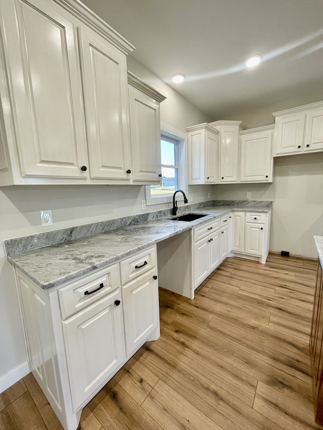 kitchen with light hardwood / wood-style floors, white cabinetry, sink, and light stone counters