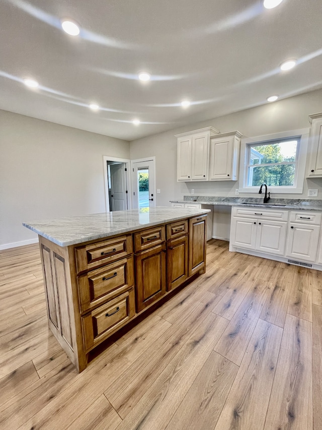 kitchen featuring white cabinets, light stone counters, light hardwood / wood-style flooring, sink, and a center island