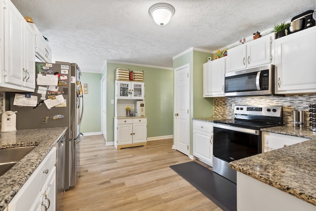 kitchen with stainless steel appliances, dark stone countertops, crown molding, light hardwood / wood-style floors, and white cabinets