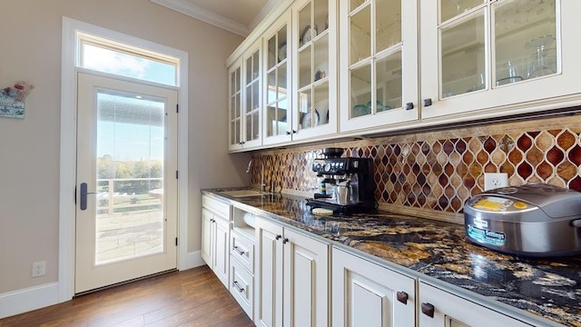 bar with decorative backsplash, dark wood-type flooring, dark stone countertops, ornamental molding, and white cabinetry