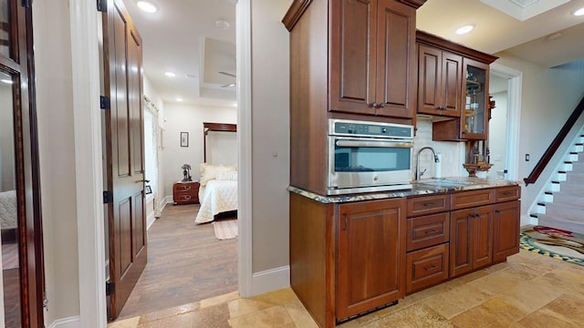 kitchen featuring oven, decorative backsplash, light stone countertops, light hardwood / wood-style flooring, and sink